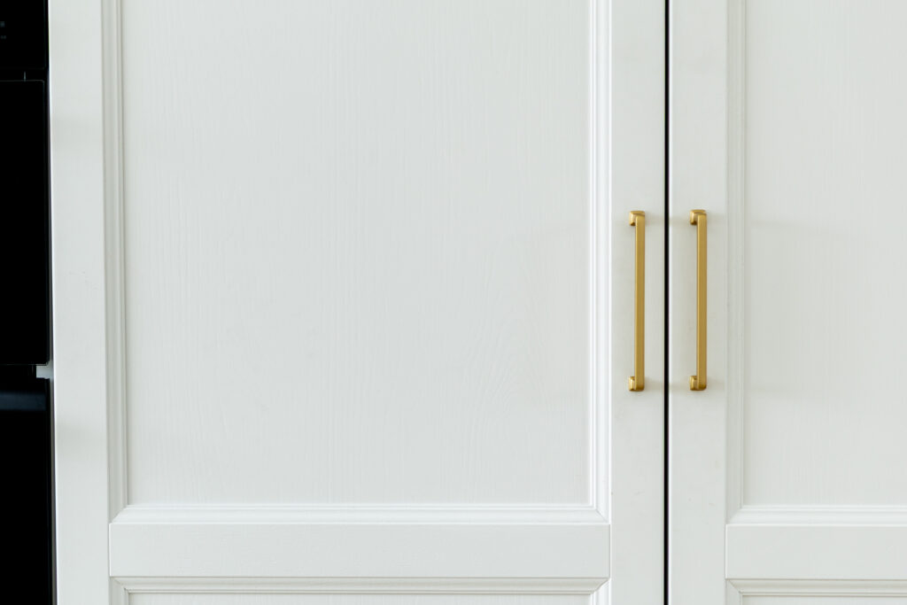 Close view of white panelled kitchen doors with brass bar handles, showing the door profile